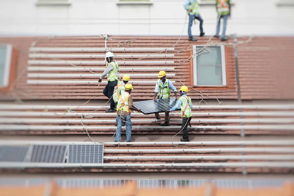 Dachdecker tragen ein Bauteil über ein frisch eingedecktes Ziegeldach